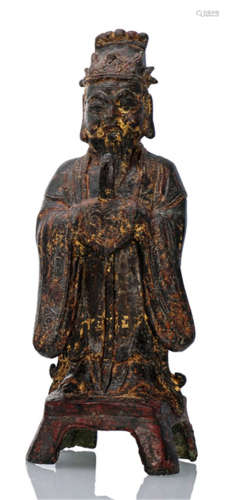 A BRONZE FIGURE OF A DAOIST OFFICIAL, CHINA, Ming dynasty, standing on a four-legged pedestal, both hands clasped in front of his breast holding a sceptre, wearing various robes including a long-sleeved mantle, his face displaying a severe expression with bushy eyebrows and topped with specific hat, traces of gilt and red lacquer-Property from an old Dutch private collection, assembled in the 1960s and 70s-Wear
