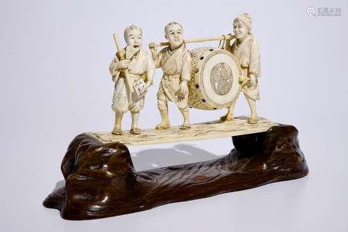 A large Japanese ivory okimono of boys playing a drum on a carved wooden base, Meiji, late 19th C., signed