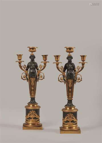 Paire de candélabres à trois lumières en bronze doré et bronze patiné, le fût en forme de femme drapée à l'antique terminée en gaine, debout sur un fût de colonne cylindrique décoré en applique d'une coupe de fruits flanquée d'une lionne de part et d'autre, la base carrée.