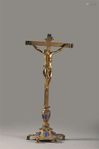 Crucifix en bronze doré reposant sur une base échancrée ornée de médaillons en cuivre émaillé bleu imitant le lapis-lazuli.