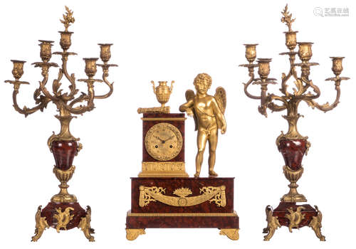 A Neoclassical mantle clock, rouge impérial marble with gilt bronze decoration and on top a leaning Cupid, mid 19thC; added a pair of ditto Rococo style candelabras, late 19thC, H 49,5 - 71 cm