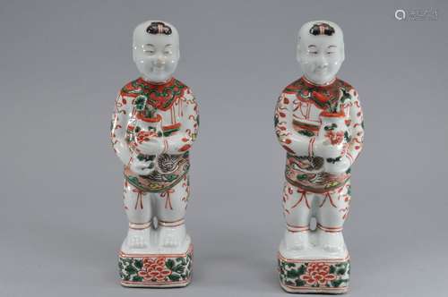 Pair of porcelain figures. China. 20th century. Standing figures of children holding lotus plants with red, green black and yellow enameled decoration. 9-1/2