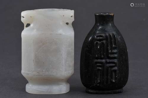 Two jade snuff bottles. China. To include: A small white octagonal vase carved with kylin and a black bottle carved with four Chinese characters. 2-1/2