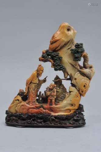 Soapstone carving. China. 18th century. Scene of a scholar with attendant in a mountain grotto. Stone of a tan colour with red markings and painted green accents. Finely carved hardwood stand. 8