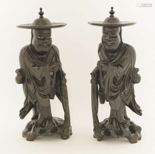 A pair of Chinese carved wood figures, early 20th century, each of a monk wearing a hat, holding a ...