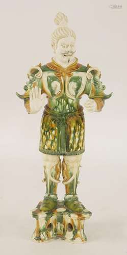 A Chinese sancai guardian figure, 20th century, in Tang style, standing on a raised platform, his ...