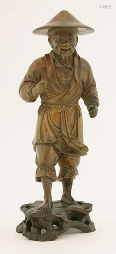 A Chinese wood carving, 20th century, of a fisherman, wearing a large hat, standing with a smile, ...