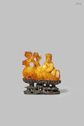 A CHINESE AMBER CARVING 19TH CENTURY Depicting a lady seated amongst rockwork beside a tree,