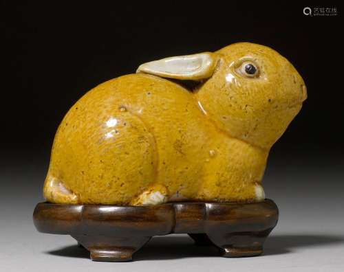 A YELLOW-GLAZED BISCUIT PORCELAIN FIGURE OF A CROUCHING HARE. China, Qing Dynasty, L 13 cm. Wooden base.