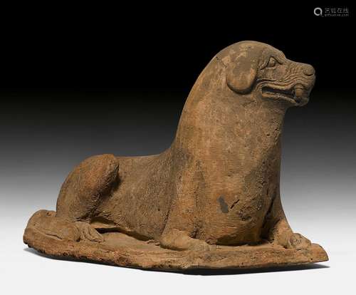 AN UNGLAZED POTTERY FIGURE OF A RECUMBENT DOG.