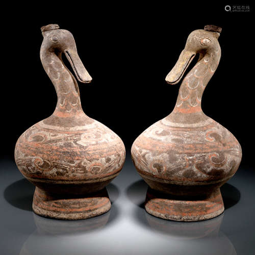 A PAIR OF PAINTED GOOSE SHAPED VASES, China, Han dynasty (206 BC - 220 AD). Each with a beak which is dramatically extended in length and size. The pouring hole on the head's top covered with a pottery lid decorated with an image of a human face. The s-shaped neck is painted with polychromes of red, white and brown. The globular body, supported by a flared out base, is decorated with two main friezes of painting of whorl patterns in red and white. Age measurement of both vases confirmed by Thermoluminescence-Analyses 20th February 2008 (Oxford Authentication, nos. C108e83 and C108e84). - Provenance: Bought in 2005 from L.H.W. Investment & Trading Limited, Hong Kong. - Described and illustrated in: Oi Ling Chiang: Collection Julius Eberhardt. Early Chinese Art, vol. 3, Hong Kong 2011, p. 74f.