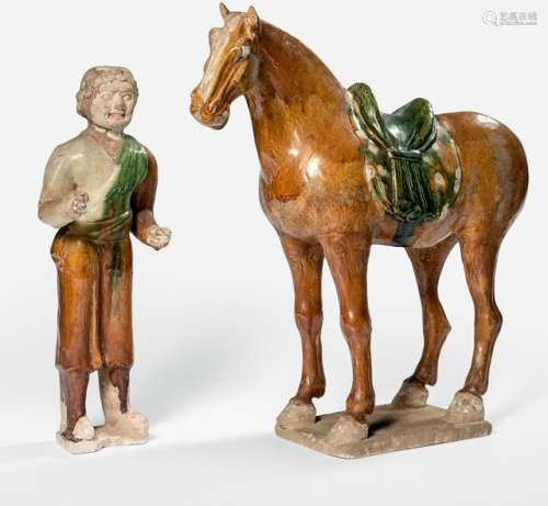 A 'SANCAI'-GLAZED HORSE AND GUIDE, China, Tang dynasty. The horse shaped in a standing position, the guide made to stand next to the horse, the right hand as if holding its leash, with a prominent smile on his face. - Property from the Emil Jannings (1884-1950) collection, Salzburg, as a gift to the present owner - The guide's right hand rest., the horse's legs rest.