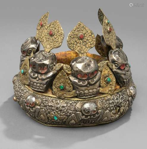 A SILVER, BRASS AND TEXTILE TIARA, TIBET, early 20th ct., the tiara consisting of a silver band embossed with five skulls set amongst foliate, the inside with brocade filling and supporting five large skulls each topped with a separate embossed ornament - Property from an old Dutch private collection, assembled from 1950 till the 1990s, by descent to the present owner - Partly chipped, wear