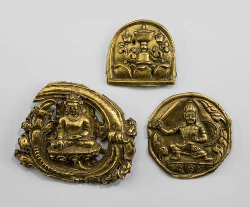 THREE GILT-COPPER EMBOSSED PLAQUES, Tibet, ca. 15th-17th ct. The largest medallion-shaped plaque with a Buddha seated in vajrasana on a lotus base with his right hand in bhumisparshamudra issued from a scrolling tendril; the second with a warrior standing on a lotus base, holding sword and shield, wearing armour and helmet; the last horse-shoe shaped plaque embossed with three butter lamps and cover standing on a lotus base. - Property from an Austrian private collection, acquired prior to 1990 - Wear, partly chipped