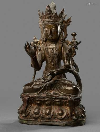 A BRONZE FIGURE OF GUANYIN, CHINA, Ming dynasty, seated in vajrasana on a lotus base with both hands holding lotus stem flowering along the upper arms, wearing dhoti, scarf, bejewelled, his face displaying a serene expression with downcast eyes and his hair combed in a chignon secured with a tiara - Property from a Rhineland-Palatinate private collection of Tibetan art - Stand slightly chipped, wear