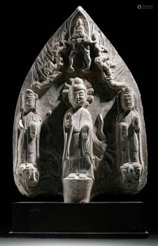 A CARVED LIME STONE MANDORLA DEPICTING BUDDHA AND TWO BODHISATTVA, China, Northern Wei dynasty (386 - 535 AD). The principal figure has a high Usnia, a lotus patterned halo and wears a broad sashed thin Kasaya, its hands in the Varada Mudras position and stands barefoot on a round pedestal. The two attendant Bodhisattvas wear high crowns with trailing ribbons and have lotus patterned halos. They are embellished with a scarf draped over their shoulders, which crosses in front of their bodies and drops from their arms and standing also barefooted on a lotus pedestal. At the top are six Apsaras. - Provenance: Bought in 2007 from J. J. Lally & Co., New York. - Described and illustrated in: Oi Ling Chiang: Collection Julius Eberhardt. Early Chinese Art, vol. 3, Hong Kong 2011, p. 82f. For a similar example see Cheng Pei-Kai: Compassion and Fascination, no. 31, in: Wenwu (2003). p. 81.