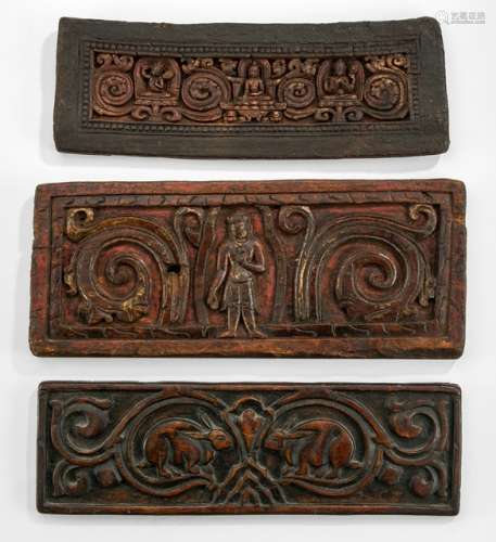 THREE WOOD MANUSCRIPT COVERS, Tibet, ca. 15th ct. and later. One carved with a pair of rabbits amongst scrolling foliage; the second with Buddha Shakyamuni in the centre, flanked by Manjushri and the four-armed Prajnaparamita, all seated on a lotus base set amongst cloud-motifs, traces of gilding; and the third sculpted with a central standing bodhisattva with both hands in varadamudra, traces of gilding - Property from an Austrian private collection, acquired prior to 1990 - Remants of red color, traces of age, some wear