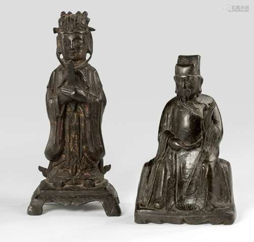 A STANDING AND A SEATED DAOIST OFFICIAL, China, 17th ct., the first bronze standing with booted feet on a shaped pedestal with both hands in front of the abdomen holding a scepter, wearing various garments including a long-sleeved mantle, his face with slit eyes and his head topped with the specific hat secured with a pin, traces of gilt and red lacquer - Property from a South German estate since at least 1985 in the property of the family - Wear, losses
