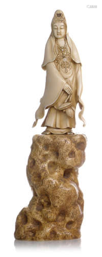 A STAINED IVORY OKIMONO OF KANNON BOSATSU WITH A LOTUS STANDING ON HIGH ROCK