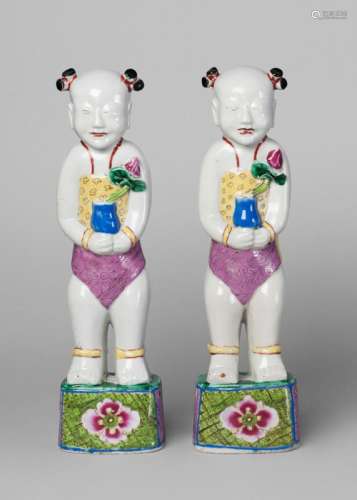 A pair of Chinese porcelain famille rose figures of boys, early 19th century, each modelled standing, smiling, holding a vase with a lotus flower, on floral painted base, 29.5cm high