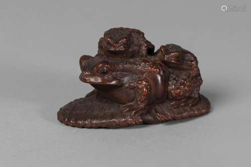 A Japanese boxwood netsuke, early 20th century, carved as three toads on a discarded sandal, signed, 6.5cm long