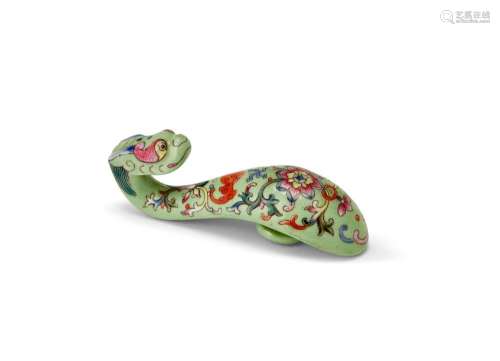 A rare Chinese porcelain belt hook, Qianlong period, terminating in a dragon's head, finely painted in famille rose enamels on a lime green ground with a bat and scrolling lotus blooms, 8.5cm long