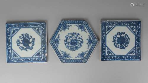 A Chinese porcelain hexagonal plaque, late 19th century, painted in underglaze blue to the centre with blossoming chrysanthemum inside six lotus flowers and a honey-comb border, 24.5cm wide, and a similar pair of square tiles, 20cm wide (3)