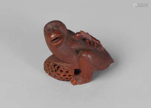 A Japanese boxwood okimono, mid 19th century, carved as a monkey leaning on a lotus pod whilst being stung by an insect, signed, 5.5cm long