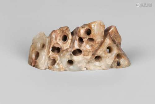 A Chinese pale green jade brush rest, early 20th century, carved as mountains, the stone of varying tone from green to brown, 12cm wide, 6cm high