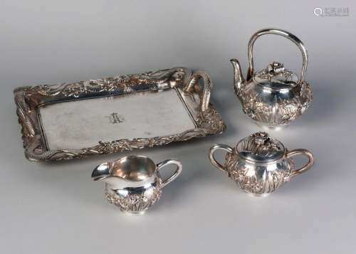 A Japanese silver three piece tea set and twin handled tray, Meiji period, the teapot, sugar bowl, and jug decorated in relief with flowering iris, the tray decorated to the rim with dragons, length of teapot 15cm, length of tray 35cm, total weight approx 50ozt (4)