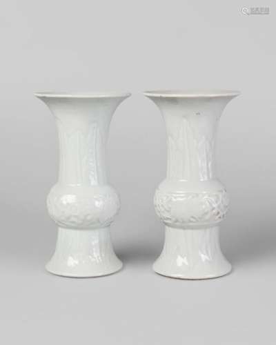 A pair of Chinese porcelain white glazed gu beaker vases, Qianlong marks, Republic period, moulded to the bulbous body with lotus flowers, and with stiff leaves to the neck, impressed seal marks and traces of paper labels to base, 17.5cm high