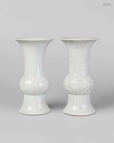 A pair of Chinese porcelain white glazed gu beaker vases, Qianlong marks, Republic period, moulded to the bulbous body with lotus flowers, and with stiff leaves to the neck, impressed seal marks and traces of paper labels to base, 17.5cm high