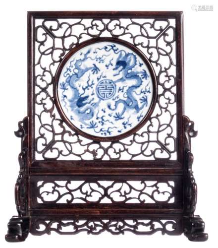 A Chinese openwork hardwood tablescreen, the porcelain plaque blue and white decorated with dragons and a Shou sign, Kangxi marked, H 36 cm (with base) - W 31,5 - D 12 cm - ø 15,5 cm