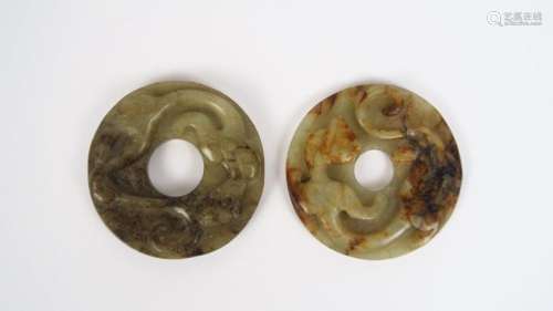 Deux disques bi en jade céladon et jade blanc veiné de rouille, sculptés de dragons déroulés sur le pourtour et de motifs géométriques au revers. <br/>Chine, XVII ème - XVIII ème siècle. <br/>Diam. 5 cm