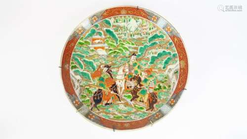 Grand plat en porcelaine d'Imari à décor en polychromie de trois guerriers à cheval se dirigeant vers un palais recouvert de neige.<br/>Japon, vers 1900.<br/>Diam. 46 cm