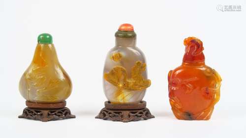 Lot comprenant trois flacons tabatières en agate et cornaline, décor de personnages sur une embarcation, bouquet de fleurs et d'arbustes en fleurs.<br/>Chine, vers 1900.<br/>H. 5,8 cm, 5,3 cm et 5,7 cm