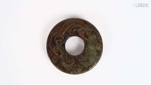 Disque bi en jade vert et brun, décor de dragons et motifs géométriques et stylisés. <br/>Chine, XIXème siècle. <br/>Diam. 6 cm
