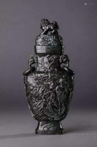 Vase couvert  sur piédouche et  col serti d'une paire d'anses zoomorphes  à anneaux mobiles et surmonté d'un chien de fô. Ciselé sur la panse d'un décor floral foisonnant. Jade vert épinard. Chine. 20ème siècle. 30,5cm. Ancienne collection de Mr Roger meffreys ambassadeur de France en Chine de 1936 à 1946