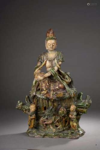 Le Boddhisattva Kwan Yin assis en délassement sur un haut tertre moulé à la base de deux attendants un dragon et un lotus, richement vêtu et paré de joyaux. Céramique vernissé sancaï, beige, brune et verte. Chine. Dynastie Ming. 1368 à 1644. Ht 46 x 34cm. Restauration. Test de thermoluminescence confirmant la datation.