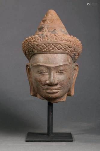 Tête de Vishnu à la beauté juvénile et l'expression sereine, les lèvres sensuelles serties d'une petite moustache exprime le sourire de béatitude typique Khmer, les yeux ciselés de simple traits, la chevelure et la barbe délicatement incisés, la coiffe composé d'un diadème noué à l'arrière et d'une mukuta conique ciselé sur trois étages. Pierre grès gris à trace d'oxydation du temps. Cambodge. Khmer. Site du Baphuon. 11 ème siècle.  Ht 24cm. Provenance ancienne collection Mr R. France 1970