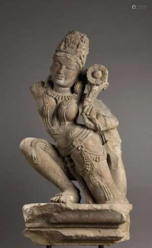 La déesse Lakshmi un genou à terre en akalasana, le buste dénudé, paré de joyaux perlé et coiffé d'une importante tiare mukuta tenant dans sa main gauche une fleur de lotus épanouie. Pierre grès gris. Inde  du Nord. 10 ème à 12 ème siècle. 85x42cm. Cassures et manque d'un bras.