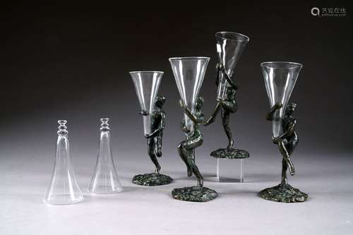 Quatre flûtes à champagne en verre portées chacune par une danseuse en bronze à patine vert sombre nuancée. Chaque pièce signée.<br/>Hauteur: environ 23 cm.<br/>On y joint deux verres “cul sec“ en verre.