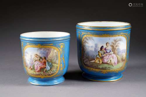 Deux Jardinières sur Piédouche. Fond bleu. Présentant chacune deux réserves figurant scène galante, nature morte et paysage, en polychromie et bordées d'or. Porcelaine française. Marque de Sèvres.<br/>Hauteur: 17 et 20 cm. Condition: Pas d'accident ni de restauration. Petits cheveux au fond d'une pièce.