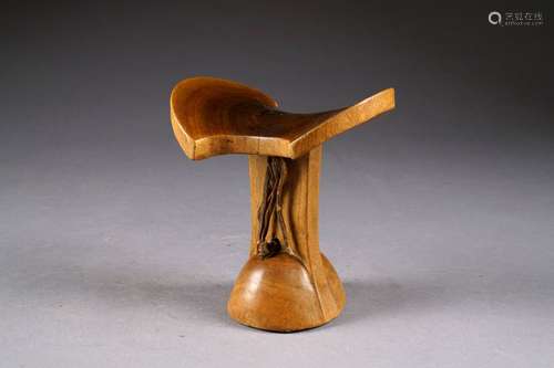 Appuie-Nuque. A plateau cambré et découpé. Lanière en cuir tressé. Bois clair sculpté à patine d'usage. Ethiopie.<br/>Hauteur: 18 cm.