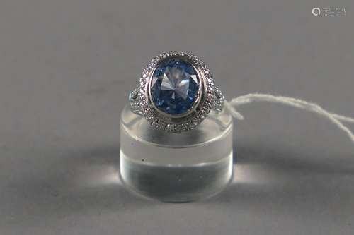 Bague de Dame “Entourage“. Sertie d'une topaze bleue taille ovale (env. 4 carats 70) rehaussée de nombreux petits zircons taille brillant. Monture en or blanc 18 carats.<br/>Poids: 8,6 g. Taille: 52.