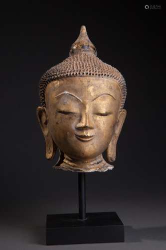 Tête de Buddha à l'expression sereine, la coiffure hérissée de bouclettes surmontée d'un rasmi piriforme.
