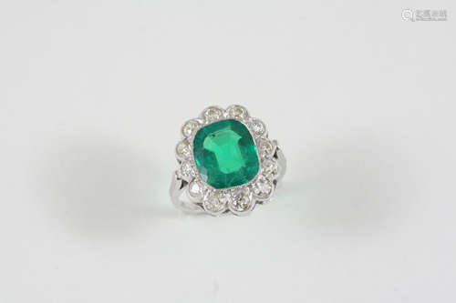 AN EMERALD AND DIAMOND CLUSTER RING the cushion-cut emerald is set within a surround of twelve