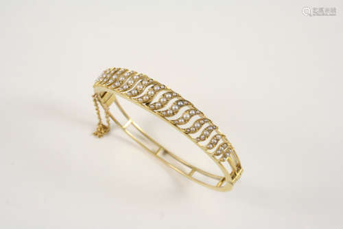A VICTORIAN 15CT. GOLD AND PEARL SET HINGED BANGLE the openwork wave design is mounted with