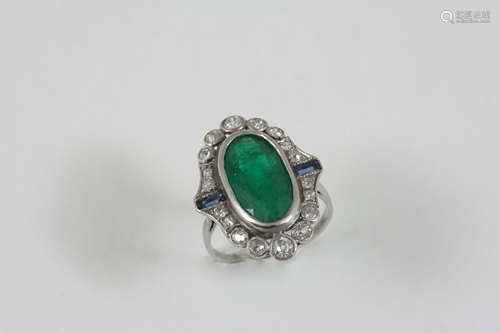 AN EMERALD, DIAMOND AND SAPPHIRE CLUSTER RING the oval-shaped emerald is set within a surround of