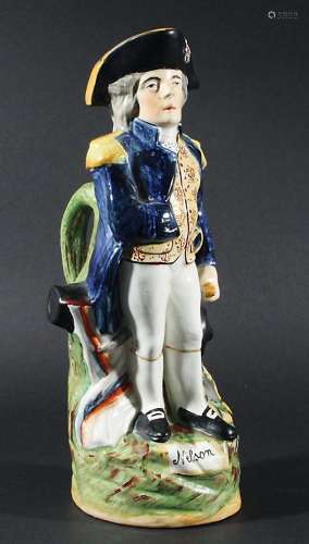 NELSON: A STAFFORDSHIRE TOBY JUG, 19th century, modelled standing before a flag and cannon, titled